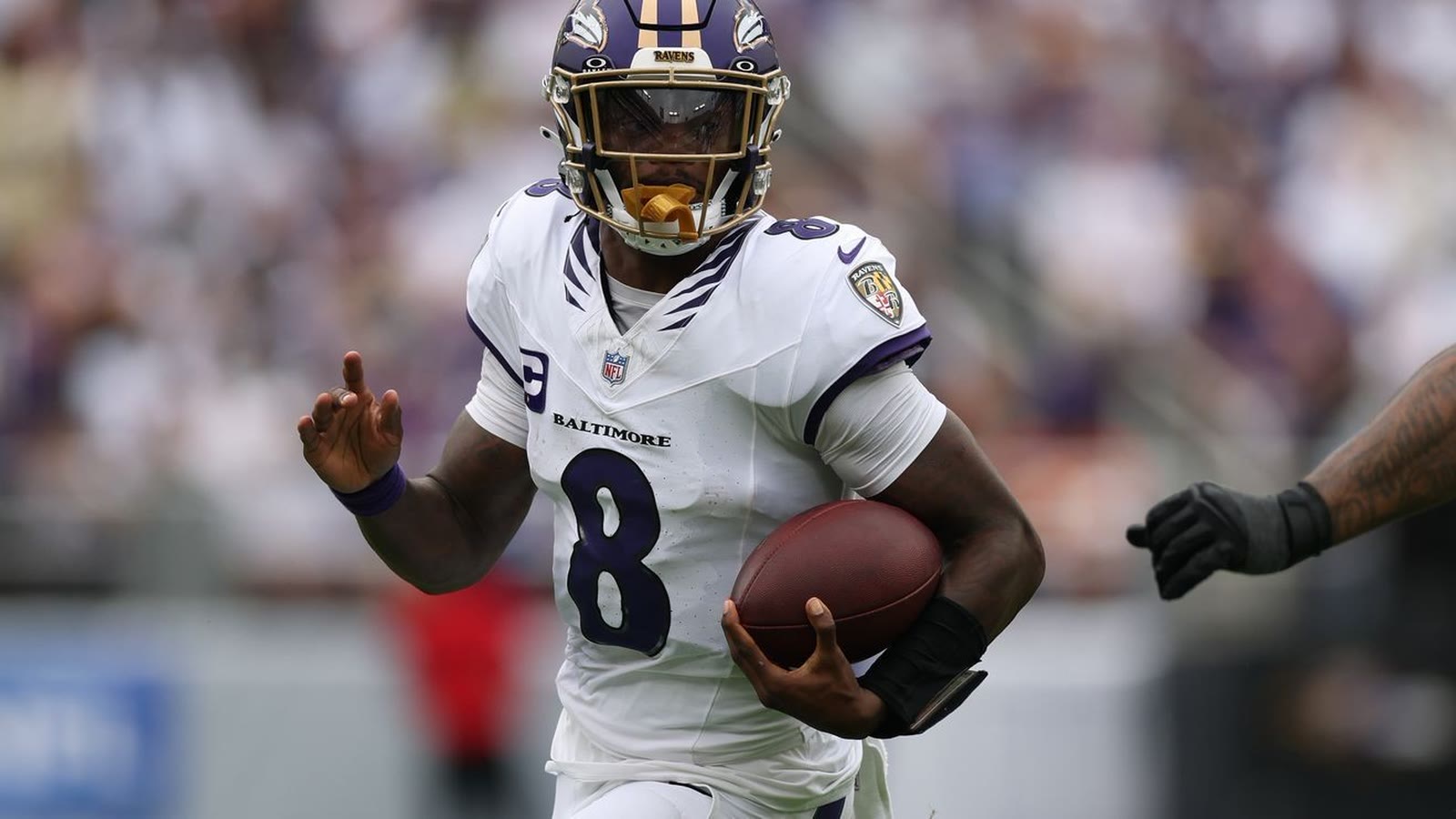 Lamar Jackson running with the ball in the Ravens white road uniform